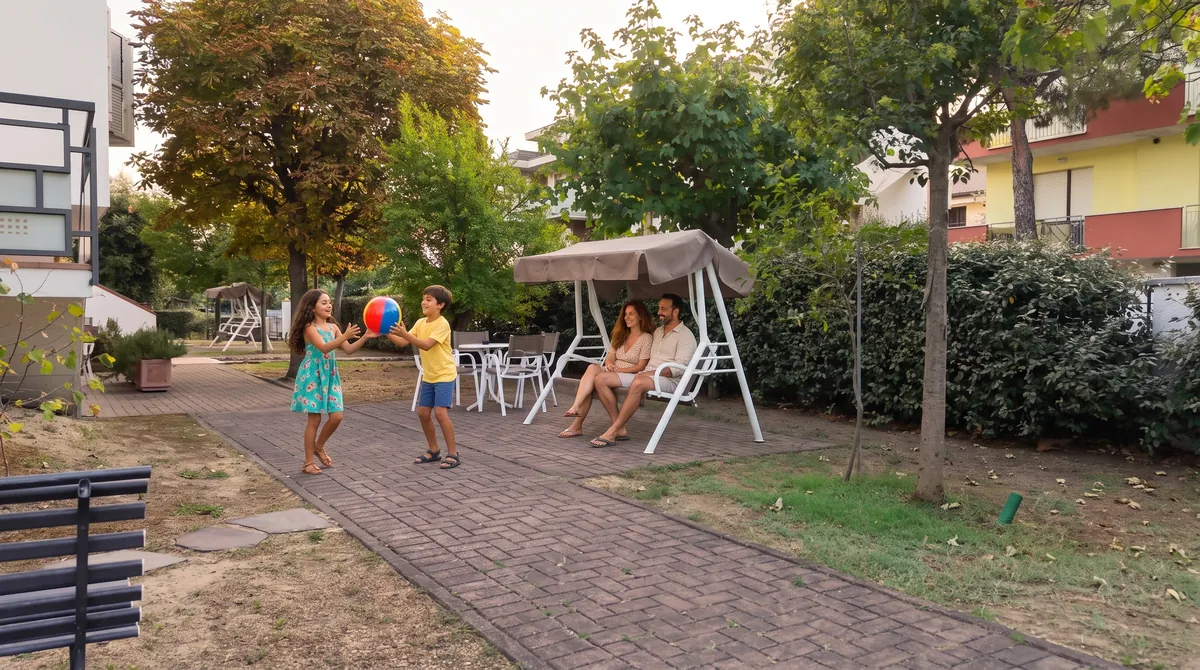 Nel giardino interno i genitori si rilassano sul dondolo e i bambini giocano a palla sul vialetto