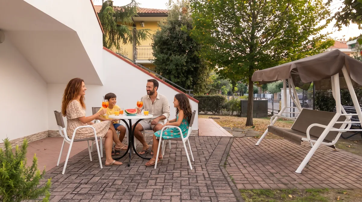 La famiglia all'aperitivo al tavolino del patio, sotto la scala, con spritz, succhi e anguria