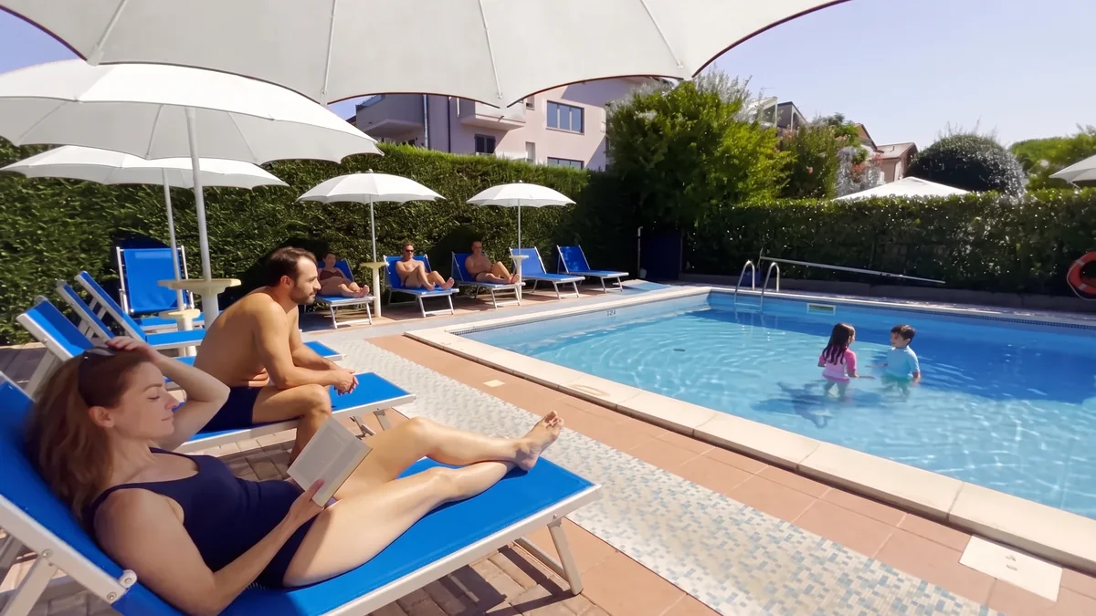 I genitori sui lettini del solarium sotto gli ombrelloni e i bambini che giocano in piscina